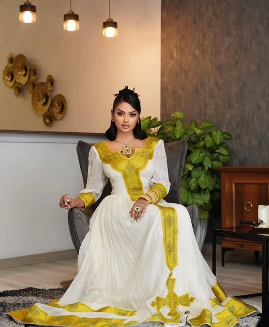 A habesha woman wearing a modern habesha dress style and sitting on a sofa for a photo shoot