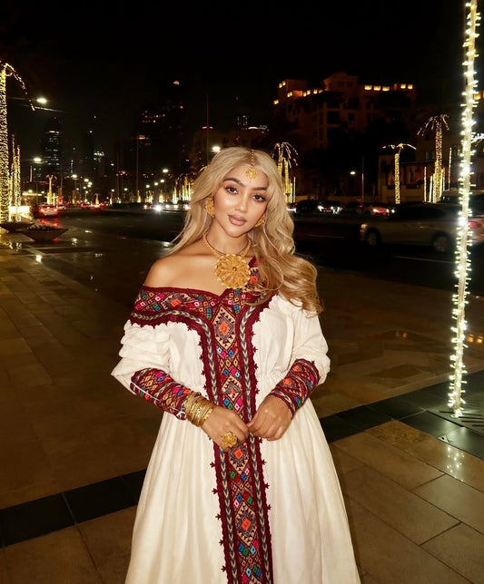 Woman in a traditional Habesha Dress with decorative patterns on a city street at night.