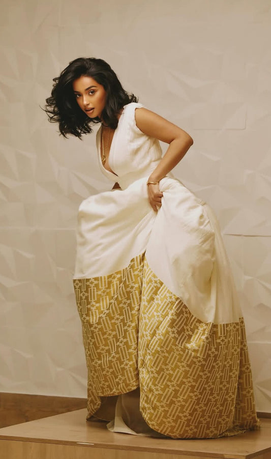 Woman wearing a white top and gold patterned pants against a plain background