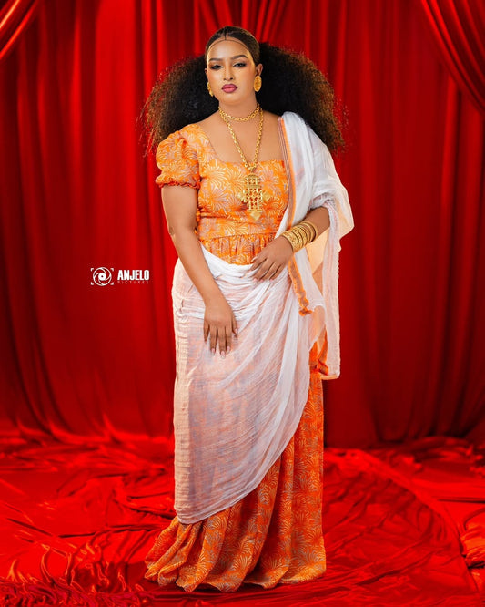 Woman in an orange and white traditional Orange Habesha Chiffon against a red curtain