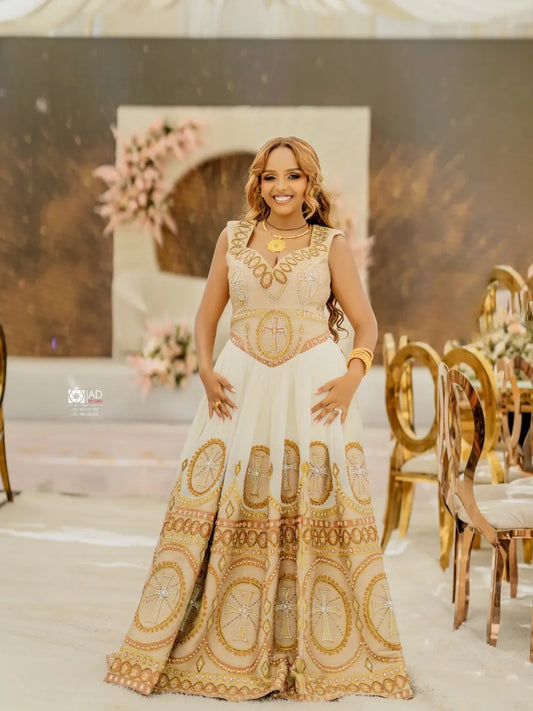 Woman in a white and gold Habesha Libs standing in an elegant indoor setting with floral decorations.