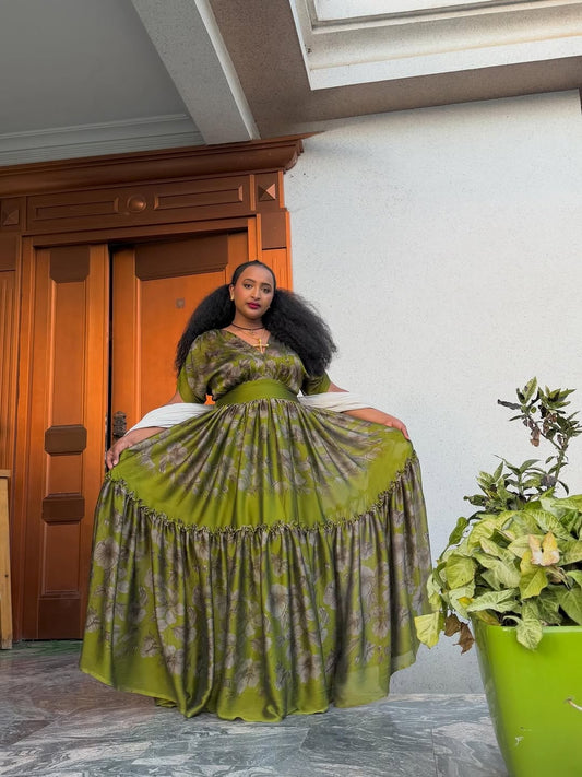Woman in a green dress standing in a room with a wooden door and potted plant.