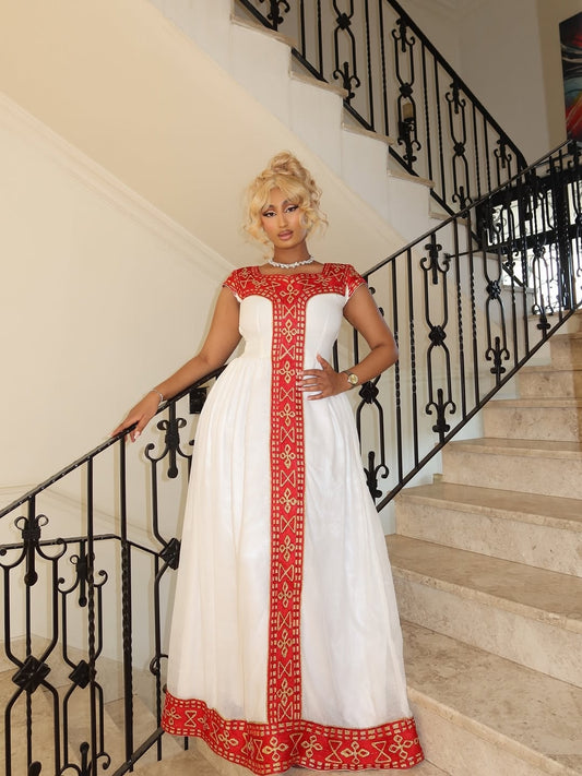 Woman in a white habesha kemis with red embroidery standing on a staircase.