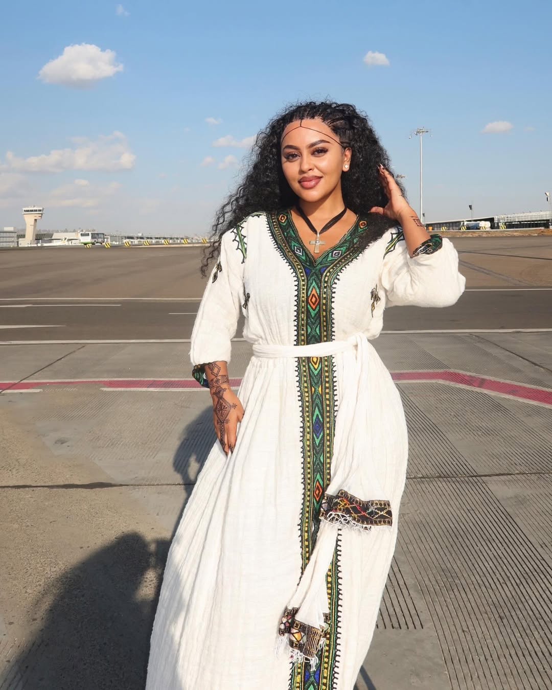 Woman in a habesha dress with colorful patterns standing on an airport tarmac.