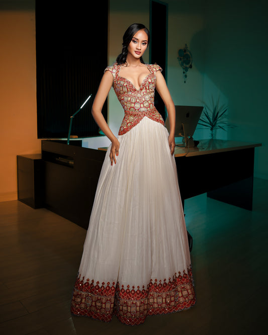 A woman models a traditional Indian evening Ethiopian National Dresses with a white pleated skirt, a heavily embellished red and gold beaded bodice, and a decorative red and gold border at the hem, set in a dimly lit modern office environment.