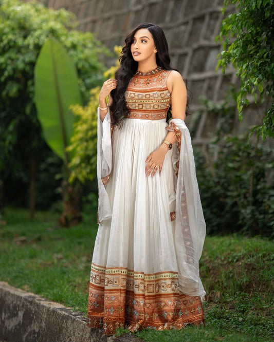 Woman in a Gold Habesha Kemis with a white and patterned dress standing outdoors.