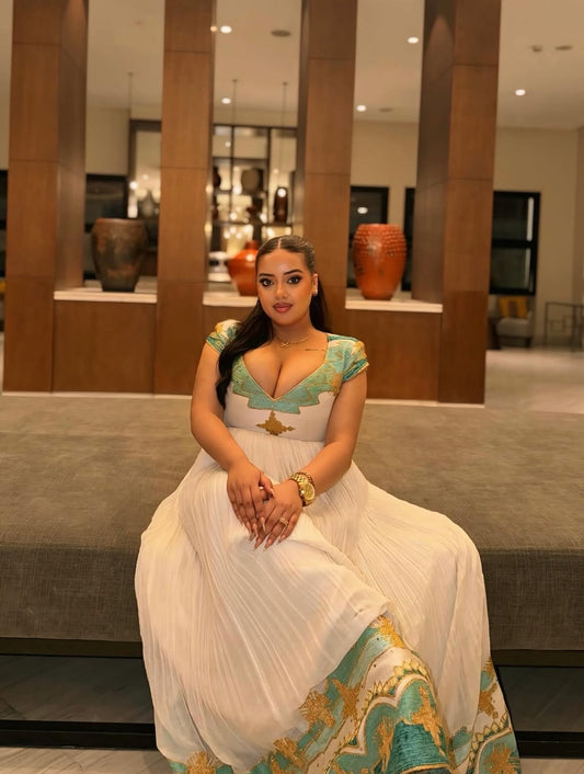 Woman in a white and traditional Green Ethiopian Dress sitting on a bench in an indoor setting.
