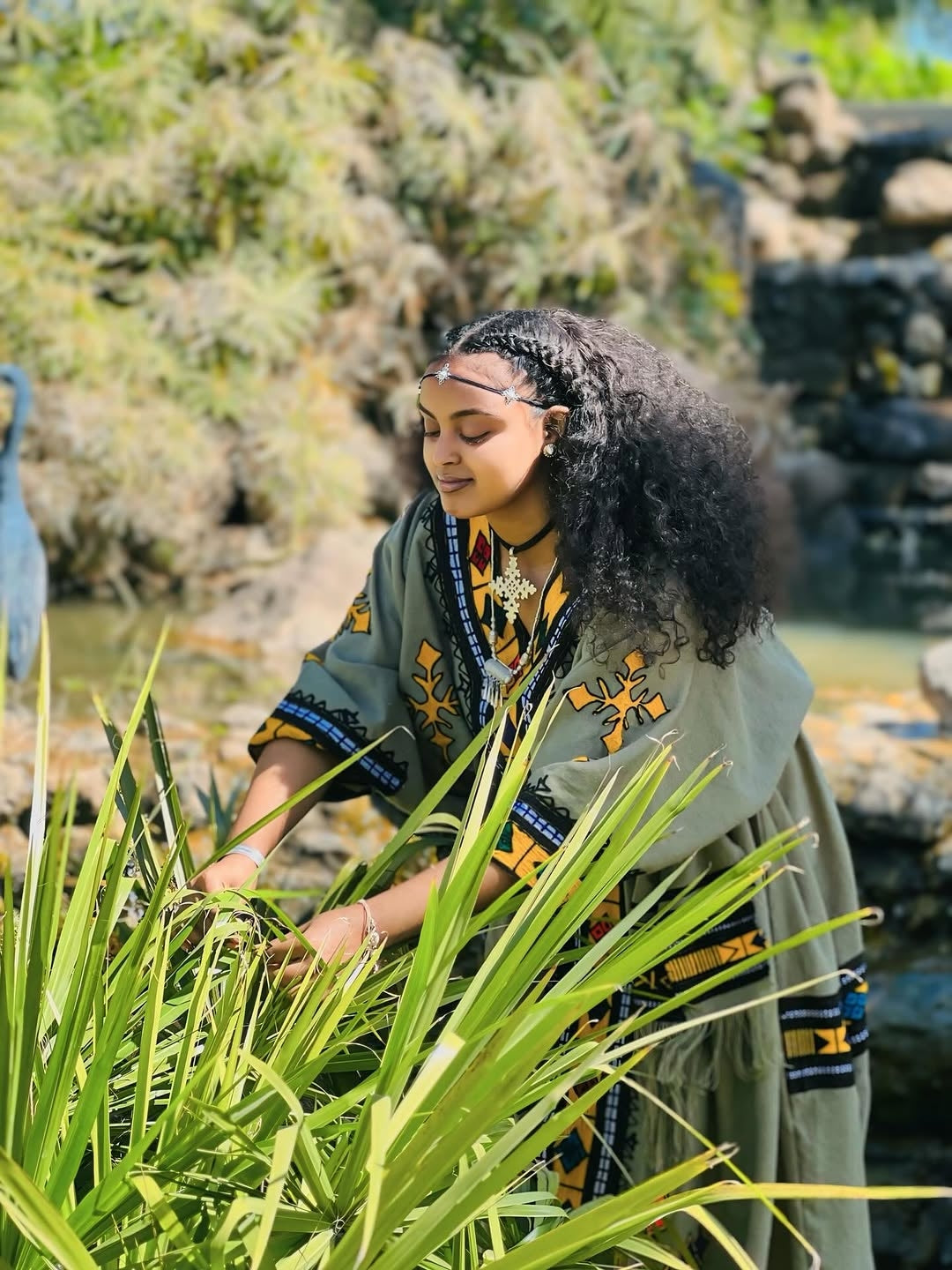 Person in traditional Ethiopian attire interacting with plants in a natural setting