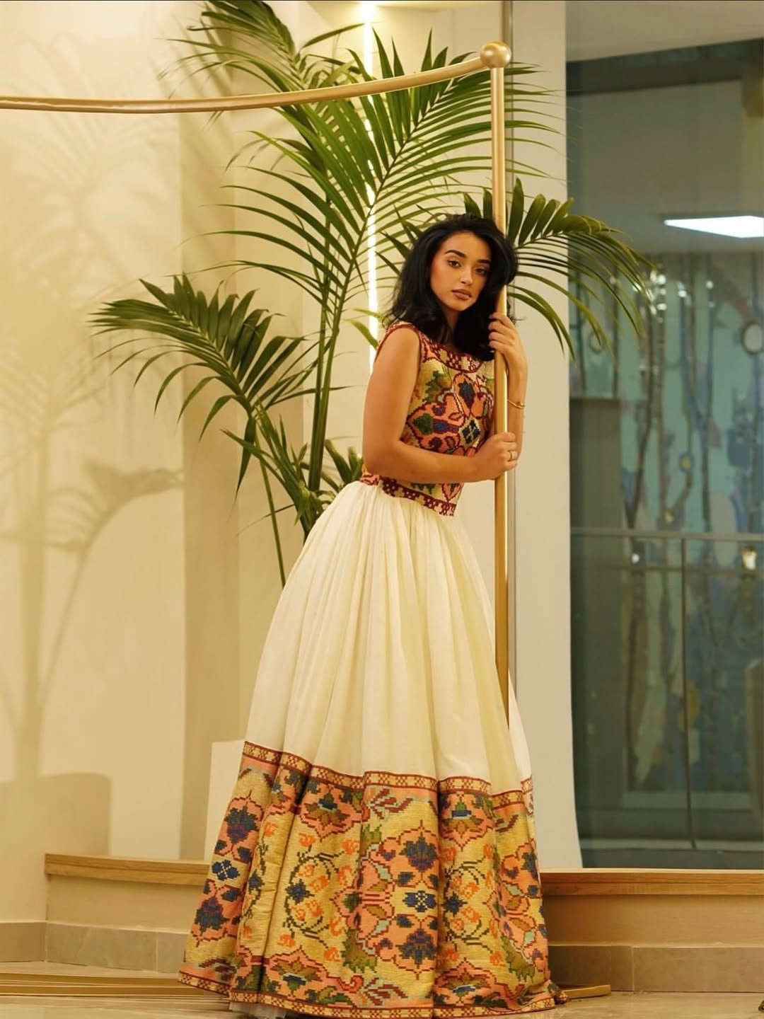 Woman in a floral Ethiopian Traditional Dress standing indoors with plants and a staircase in the background