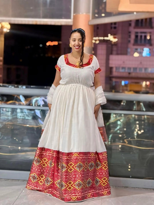Woman wearing a white Ethiopian Dress with red and gold patterns in an indoor setting.