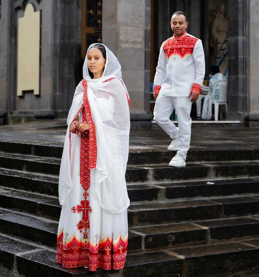 Two people in white and red Traditional Habesha Dress attire standing on steps outside a building.