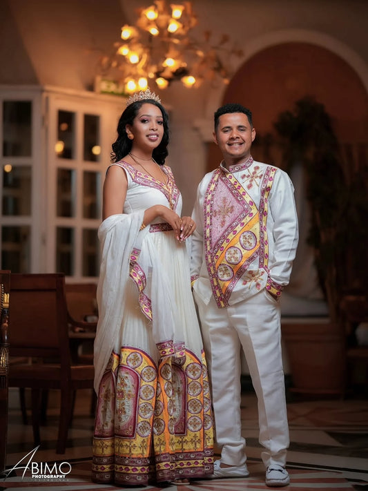 Man and woman in Ethiopian Wedding Outfit attire standing together in a decorated room with chandelier.