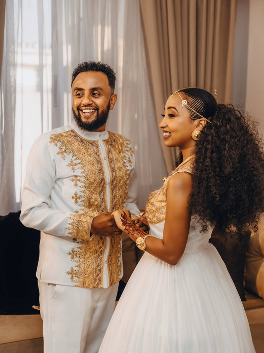 Man and woman in formal Gold Ethiopian Matching Couple Wedding Set standing close together indoors.