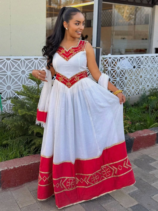 Woman wearing a white and red traditional outfit with gold accents outdoors.