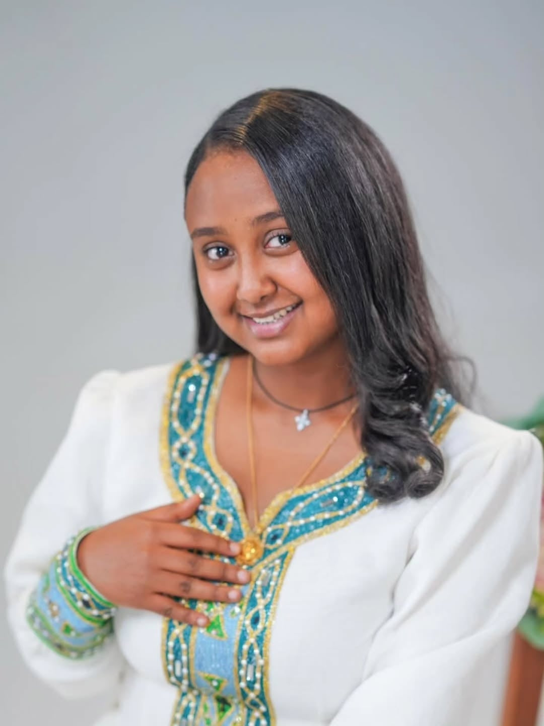 Woman wearing a traditional Green Habesha Kemis with intricate designs on a plain background