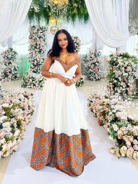 Woman in a white and patterned habesha zuria standing in front of floral decorations