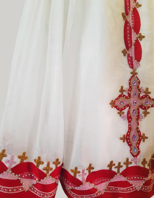 White fabric garment with prominent red and gold embroidered Ethiopian Outfit, including a large cross motif and decorative trim along the hem.