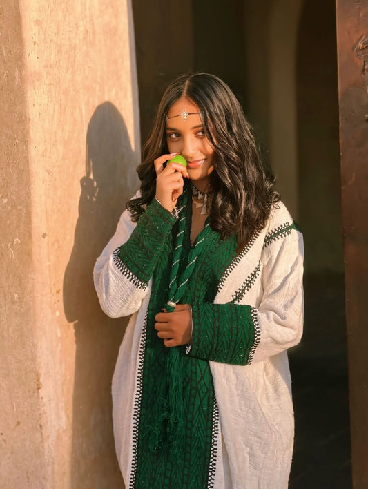 Woman wearing a green and white traditional Ethiopian dress against a textured wall.