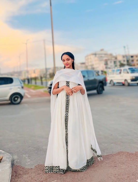 Woman in a white Traditional Dress with black patterns standing on a street.