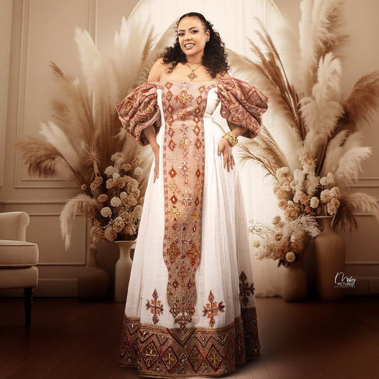 Woman in an ornate Ethiopian Dress standing in a decorated room with pampas grass and flowers.