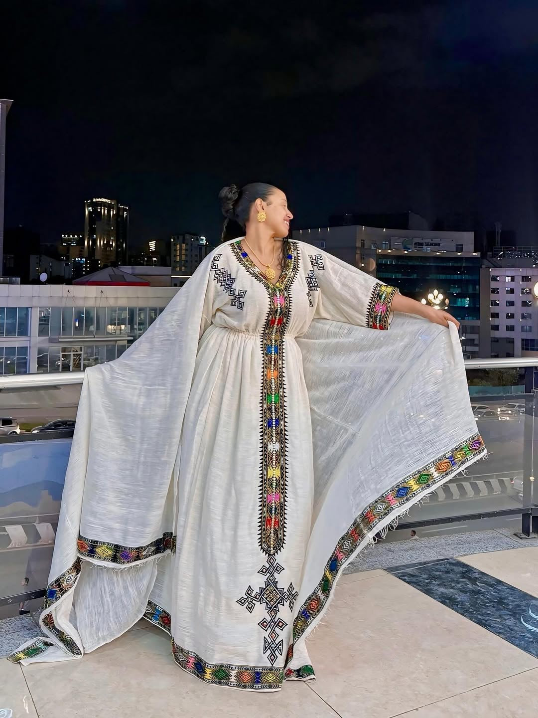 Woman wearing a traditional embroidered Ethiopian Dress on a rooftop at night.