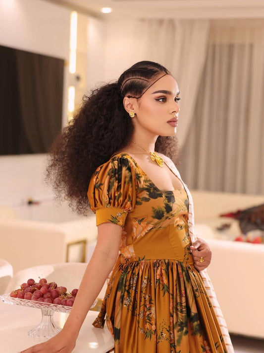 Woman in a yellow floral Gold Habesha shiffon Dress standing in an indoor setting
