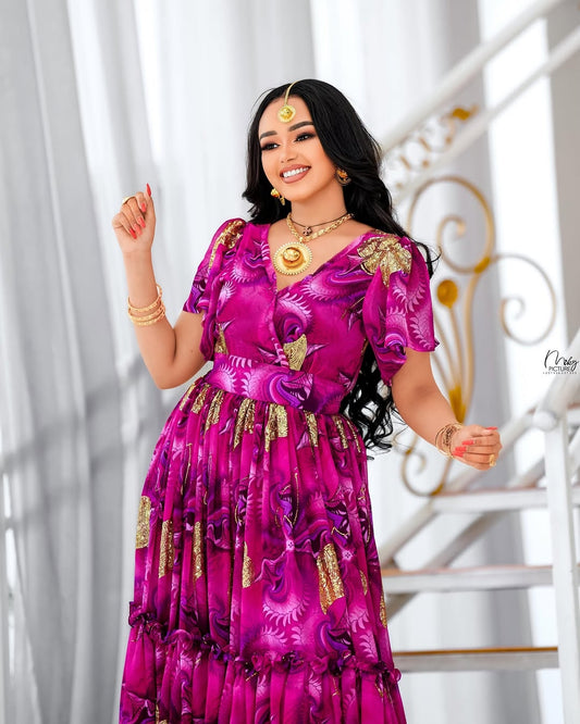 Woman in a vibrant pink traditional habesha chiffion with gold accents, posing indoors.