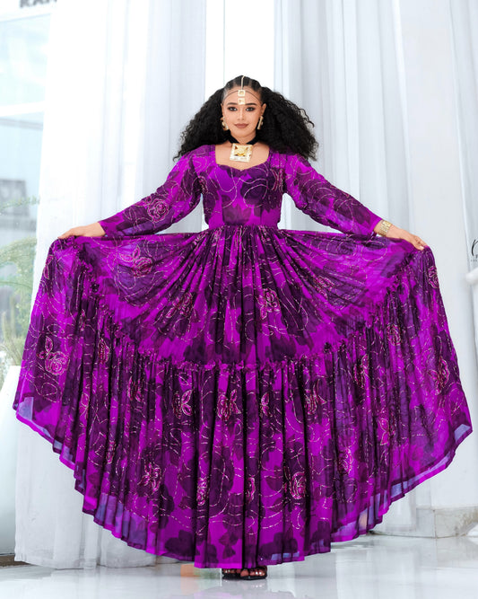 A woman modeling a vibrant purple long-sleeve Habesha chiffon with a tiered ruffled skirt, holding the fabric outwards to show its volume against a bright white curtain background.