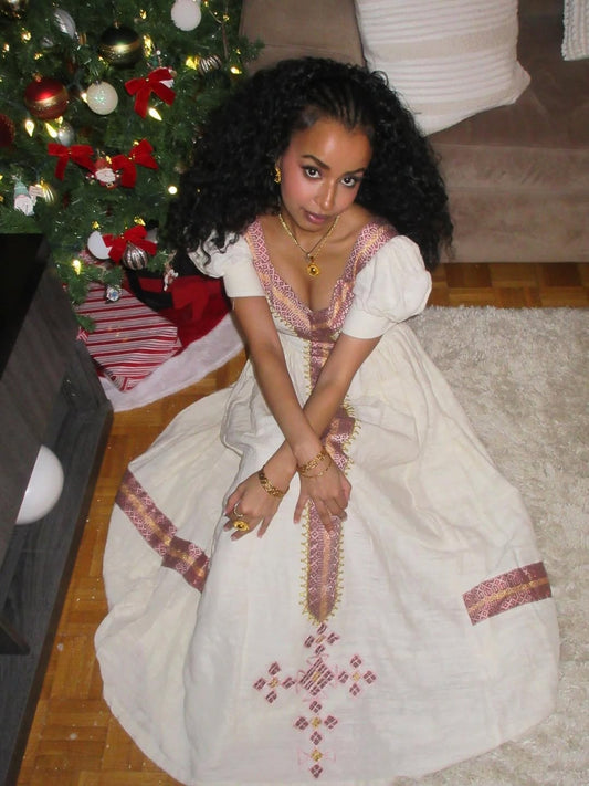 Woman in a white Habesha Libs
with red patterns sitting in front of a decorated Christmas tree.