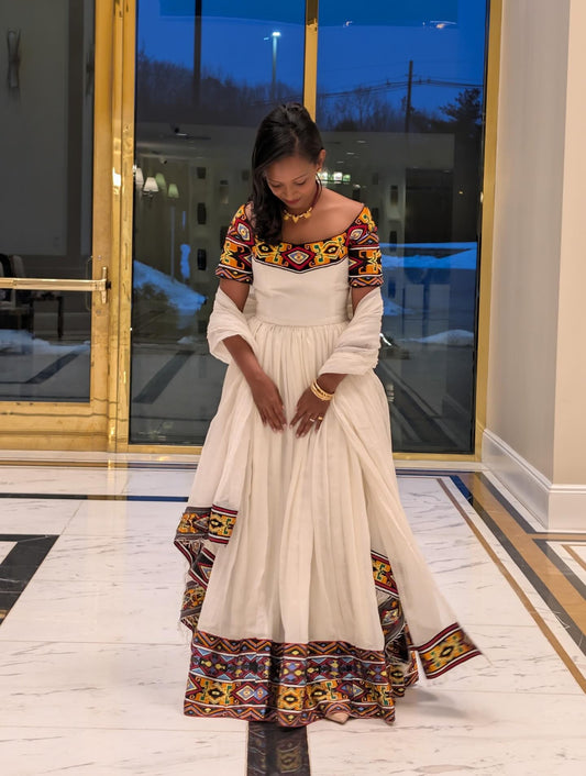 Woman in a traditional Ethiopian Traditional Dress standing in a room with large windows.