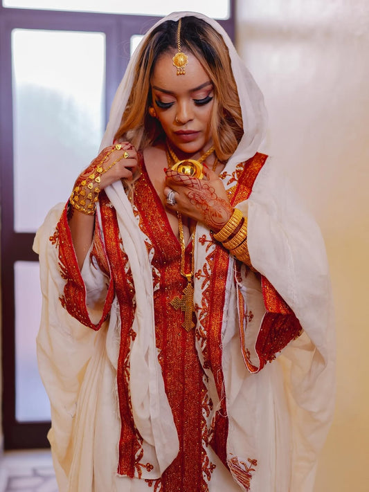 Woman in Habesha Zuria red and white saree with jewelry indoors