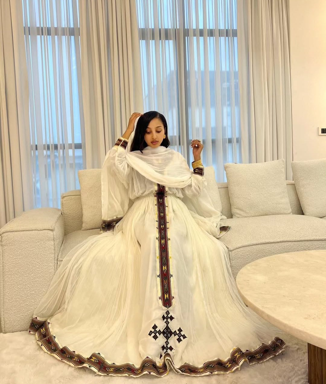 A woman dressing in her first habesha dress and sitting on a white sofa