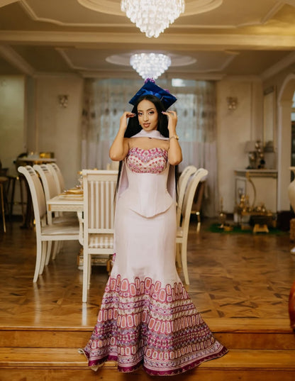 Woman in a patterned Habesha Dress standing in a decorated room with chandeliers.
