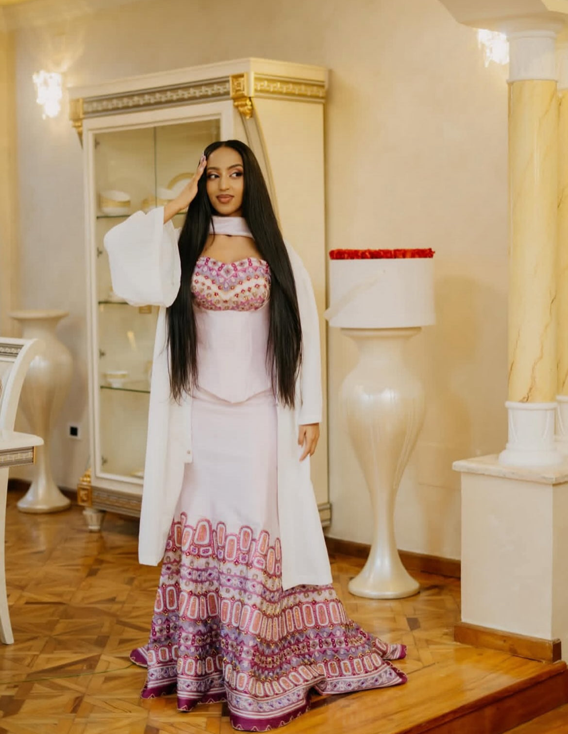 Woman in a patterned Habesha Dress standing in an elegant interior setting