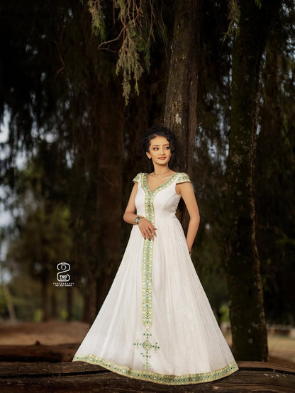 Woman in a white Green Ethiopian Traditional Dress with green embroidery standing outdoors against a tree.