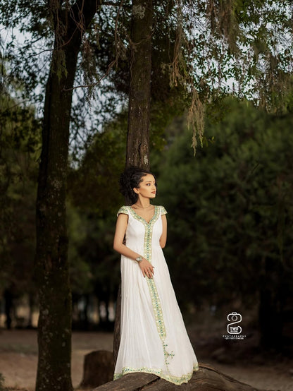 Woman in a white Green Ethiopian Traditional Dress with green accents standing in a forest setting
