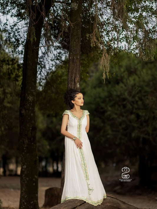 Woman in a white Green Ethiopian Traditional Dress with green accents standing in a forest setting
