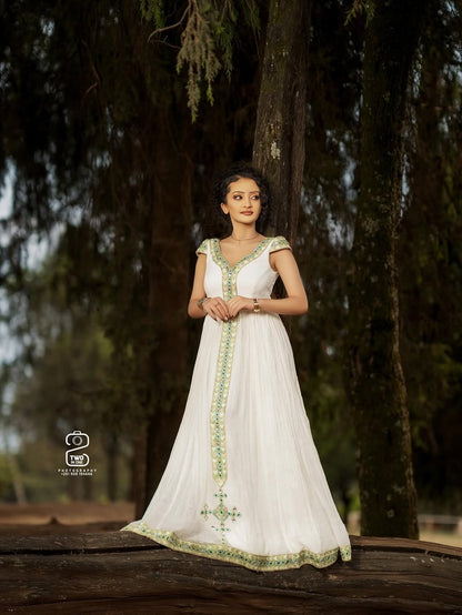 Woman in a white Green Ethiopian Traditional Dress with green embroidery standing in a forest setting