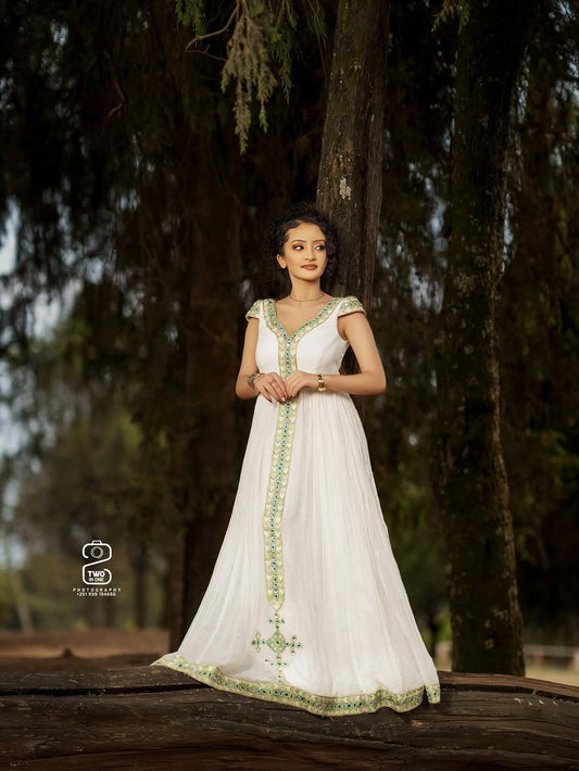 Woman in a white Green Ethiopian Traditional Dress with green embroidery standing in a forest setting