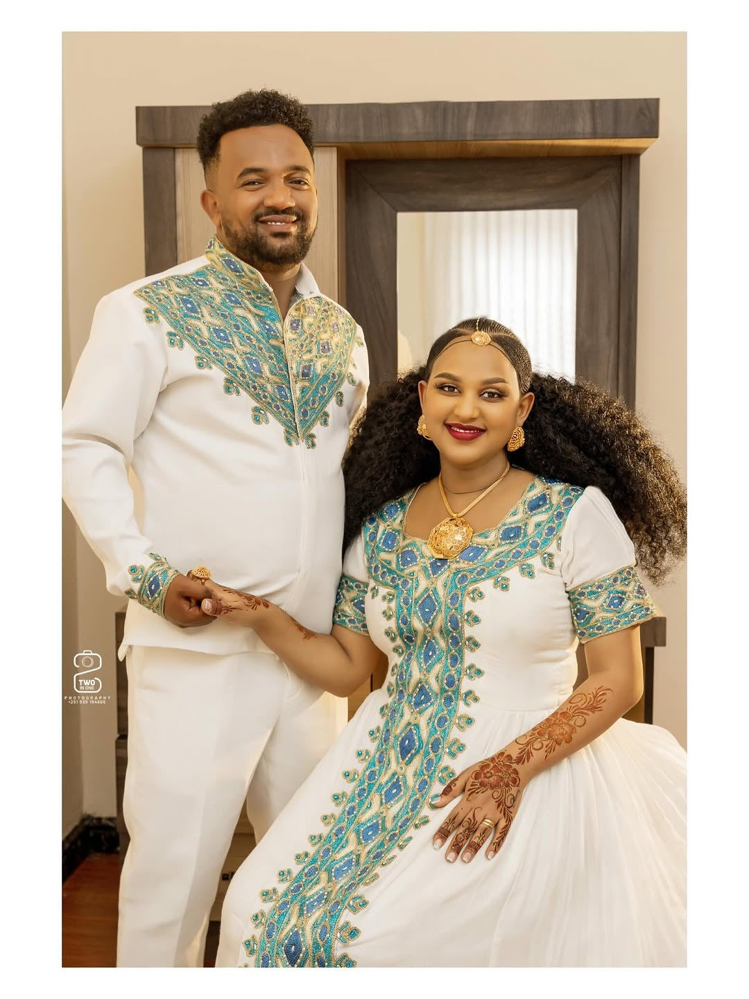 Man and woman in traditional embroidered outfits standing together indoors.