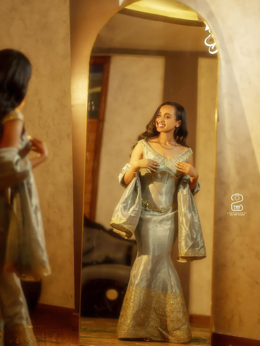 Woman in a silver and gold Green Mermaid Habesha Libs at herself in a mirror.