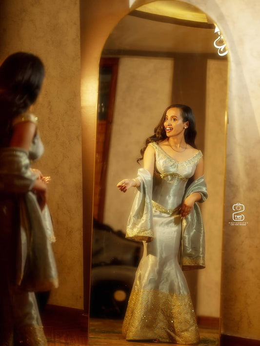 Woman in a silver and gold dress standing in front of a mirror.