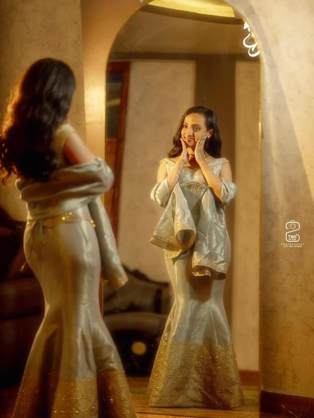 Woman in a silver dress standing in front of a mirror, adjusting her hair.