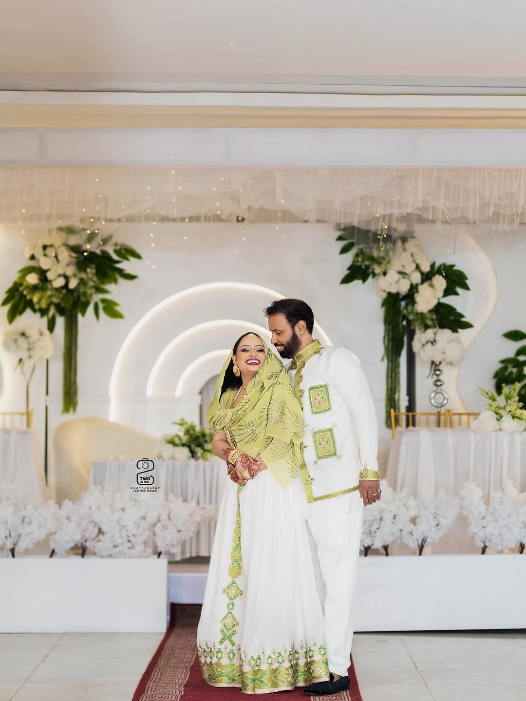 Couple in formal attire standing in a decorated indoor setting with floral arrangements.