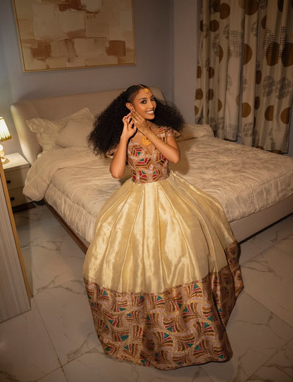Woman in a patterned Habesha wedding Dress sitting on a bed in a bedroom.