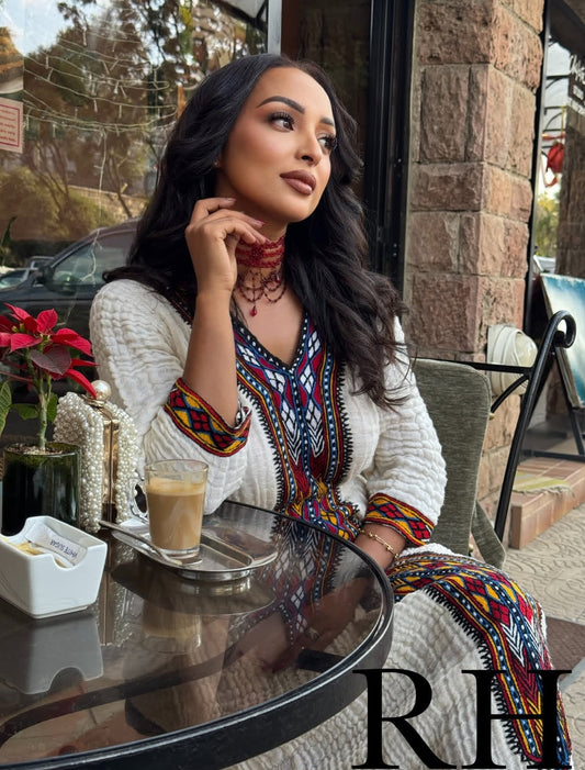Woman sitting at an outdoor cafe table with a drink, wearing a colorful Traditional Ethiopian Dress.