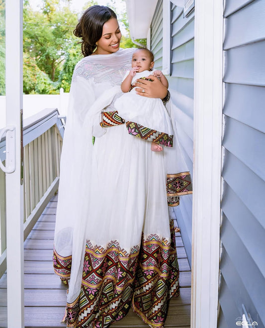Woman holding a baby wrapped in a white cloth with colorful patterns on a wooden deck.