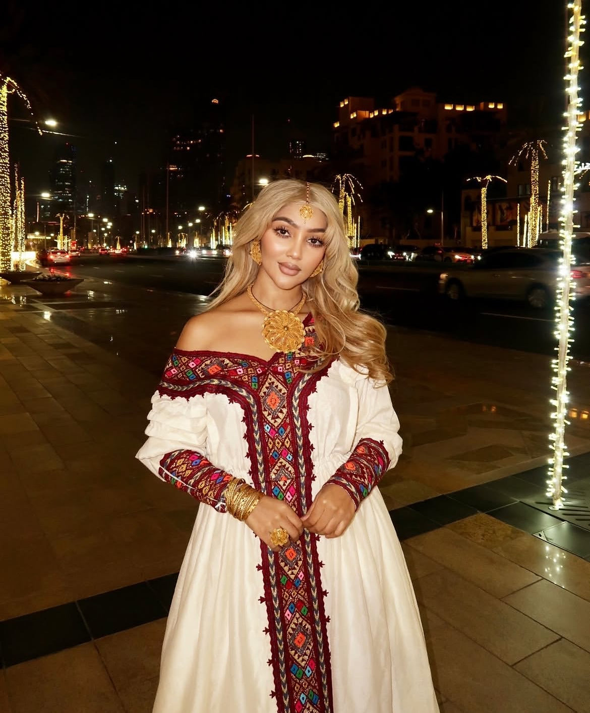 Woman in a traditional Habesha Dress with decorative patterns on a city street at night.