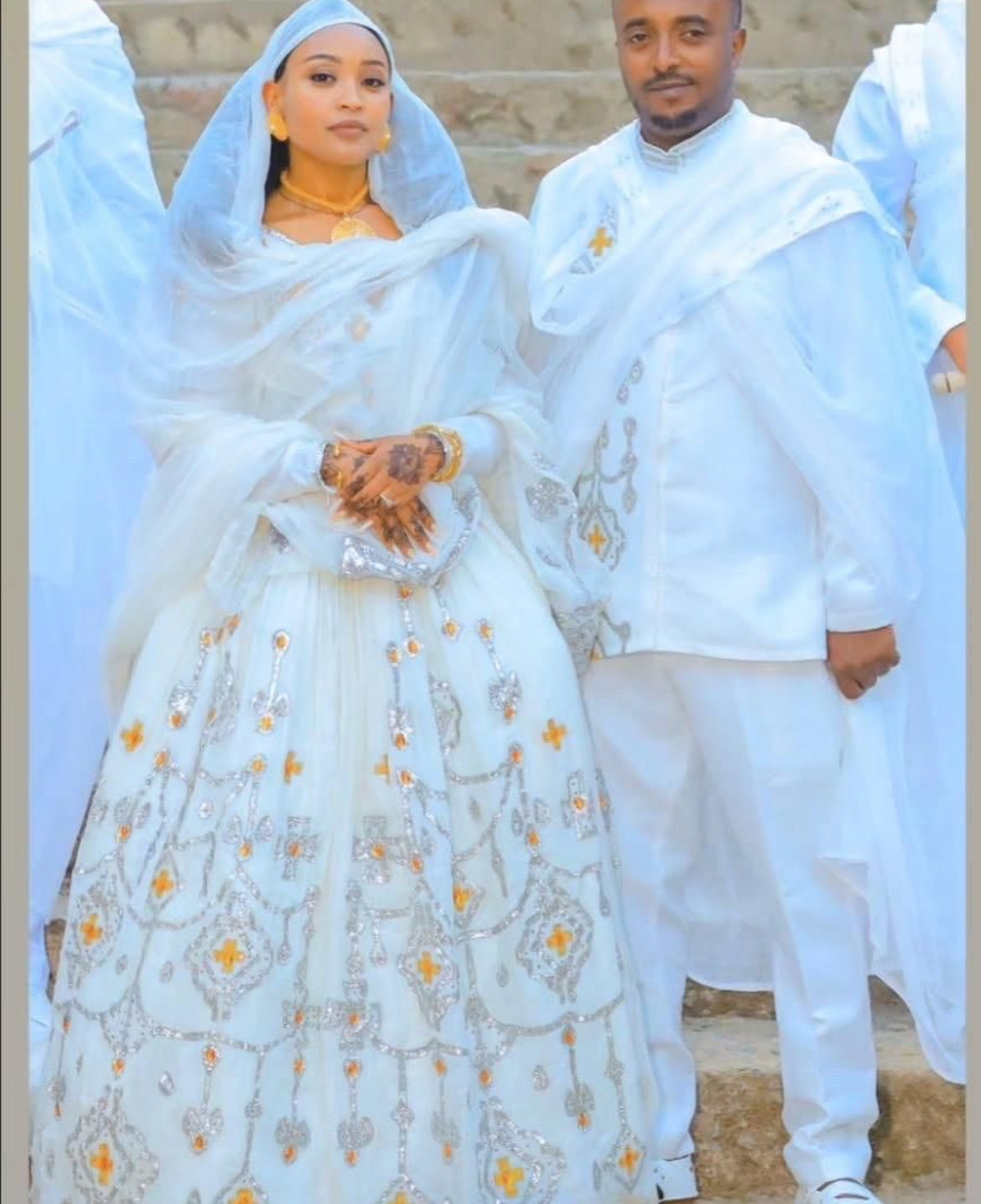 Couple in traditional white attire with floral patterns, standing close together.