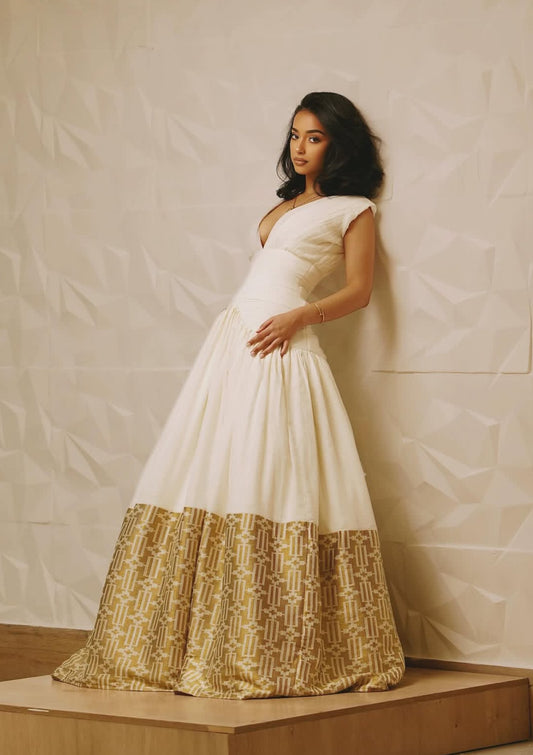 Woman wearing a white and gold dress against a plain background